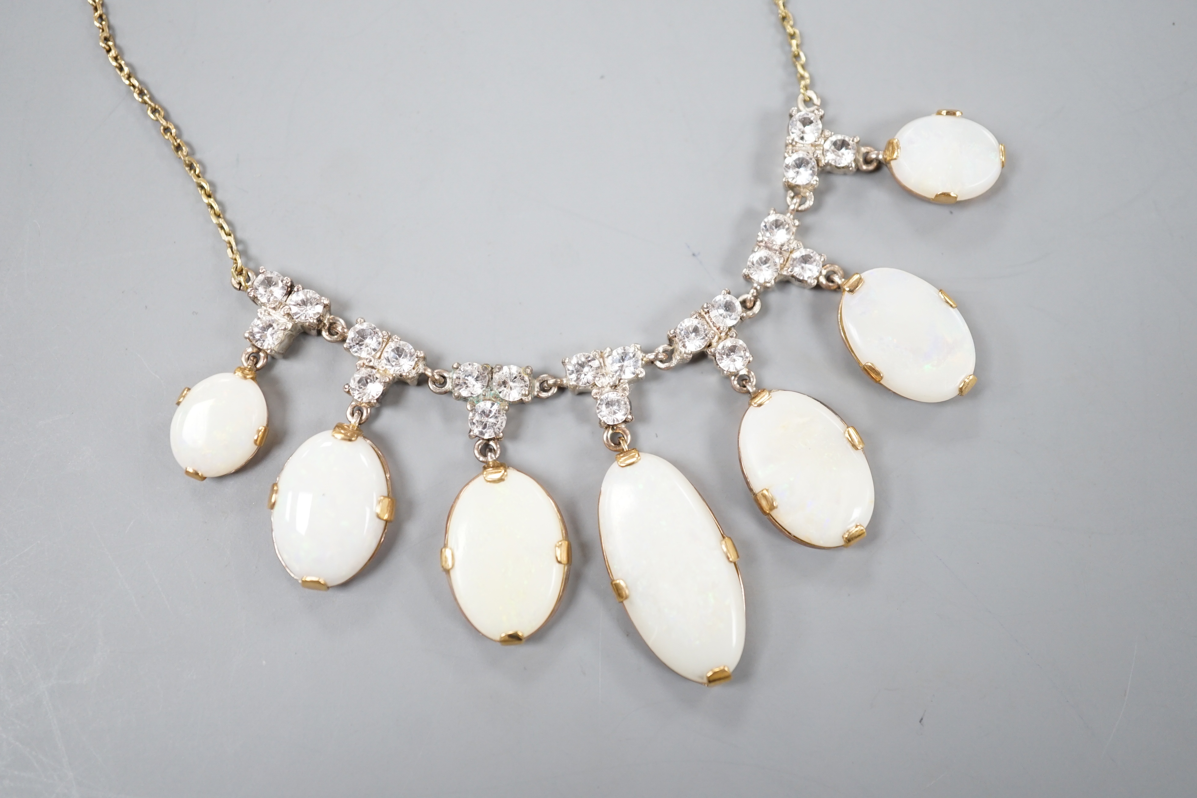 A yellow metal, graduated seven stone oval white opal and paste set cluster fringe necklace, 42cm, gross 14.6 grams.